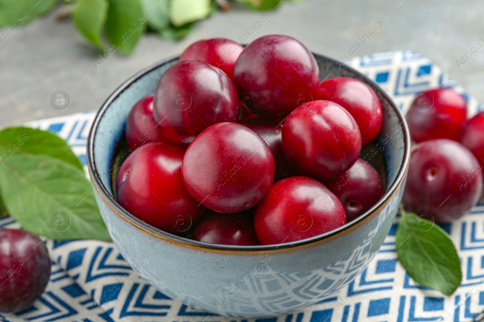 Photo of Tasty ripe plums in bowl on grey table, closeup