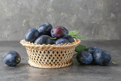 Photo of Tasty ripe plums in wicker bowl on grey textured table