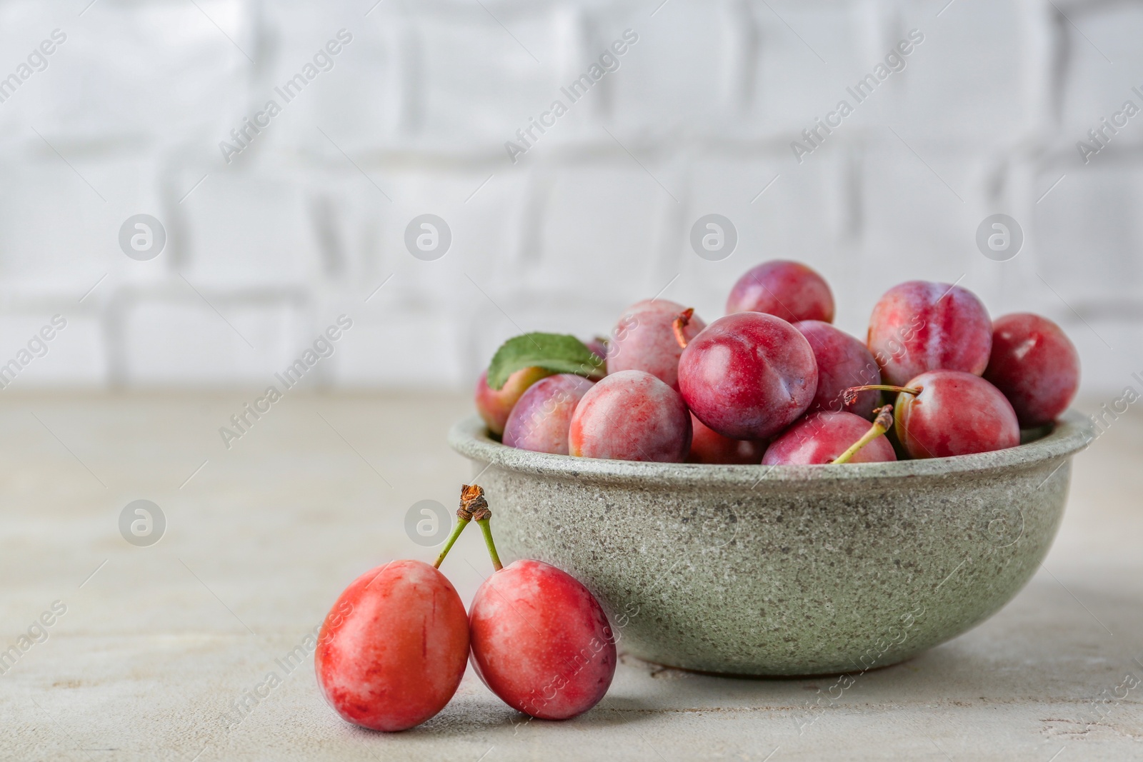 Photo of Tasty ripe plums in bowl on grey textured table, closeup. Space for text