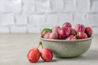 Photo of Tasty ripe plums in bowl on grey textured table, closeup. Space for text