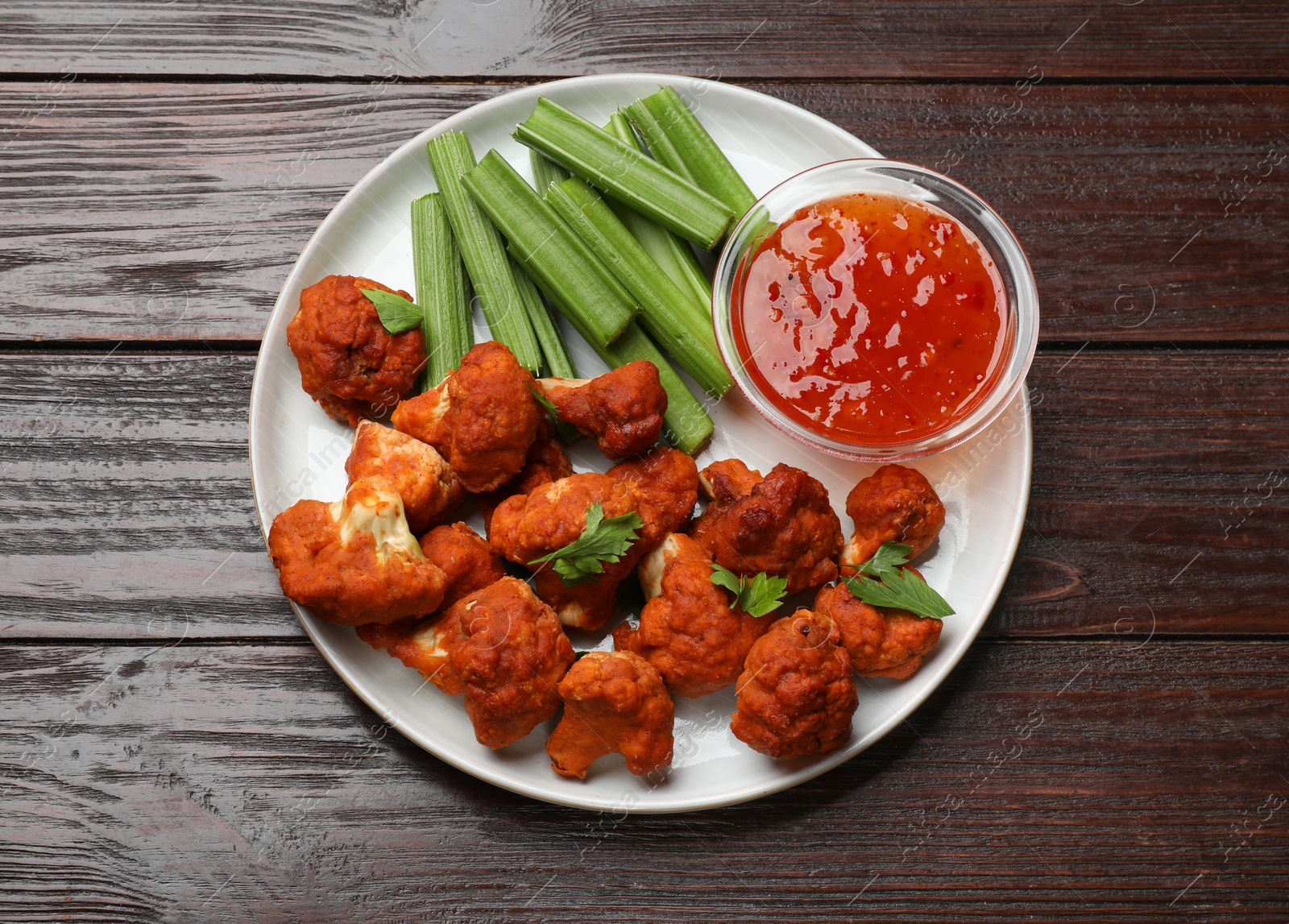 Photo of Baked cauliflower buffalo wings with celery and sauce on wooden table, top view