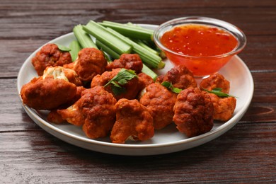 Photo of Baked cauliflower buffalo wings with celery and sauce on wooden table, closeup