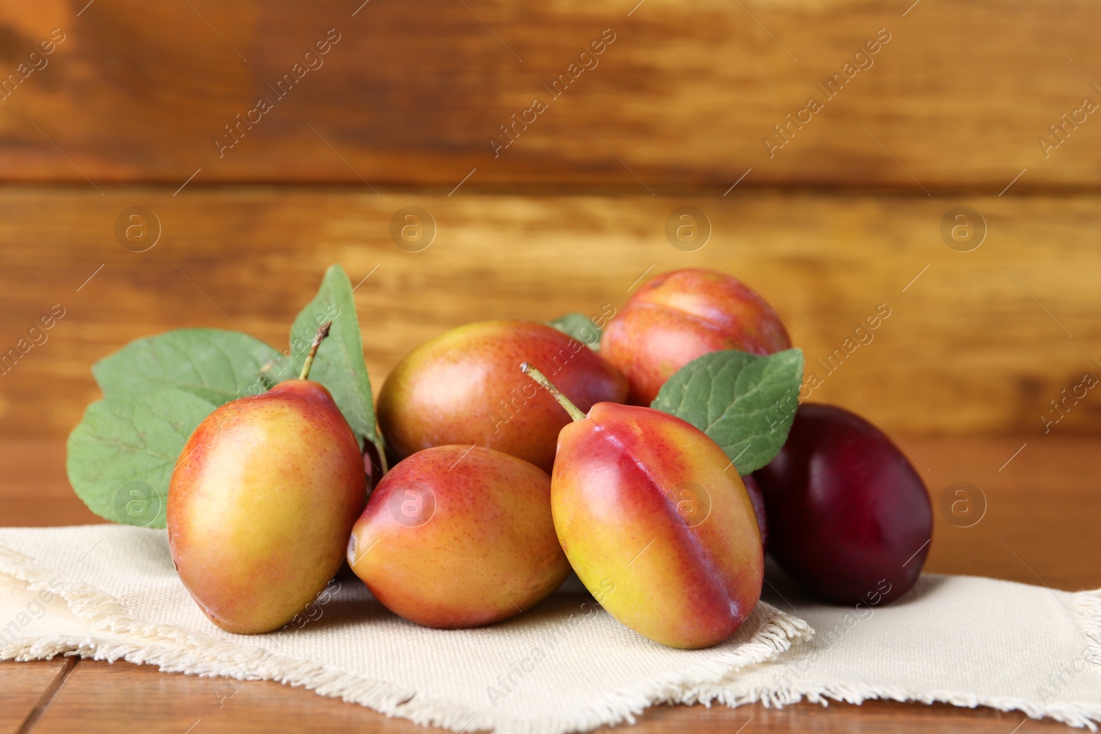 Photo of Ripe plums and leaves on wooden table, closeup