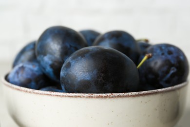 Photo of Ripe plums in bowl on table, closeup