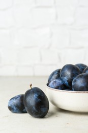 Photo of Ripe plums in bowl on light textured table