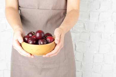 Photo of Woman holding bowl of ripe plums against white background, closeup