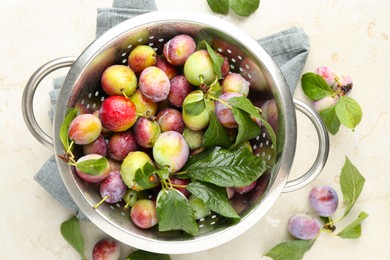 Photo of Ripe plums and leaves in colander on light table, flat lay