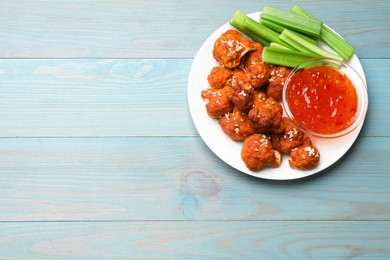 Photo of Tasty cauliflower buffalo wings, sauce and celery on light blue wooden table, top view. Space for text