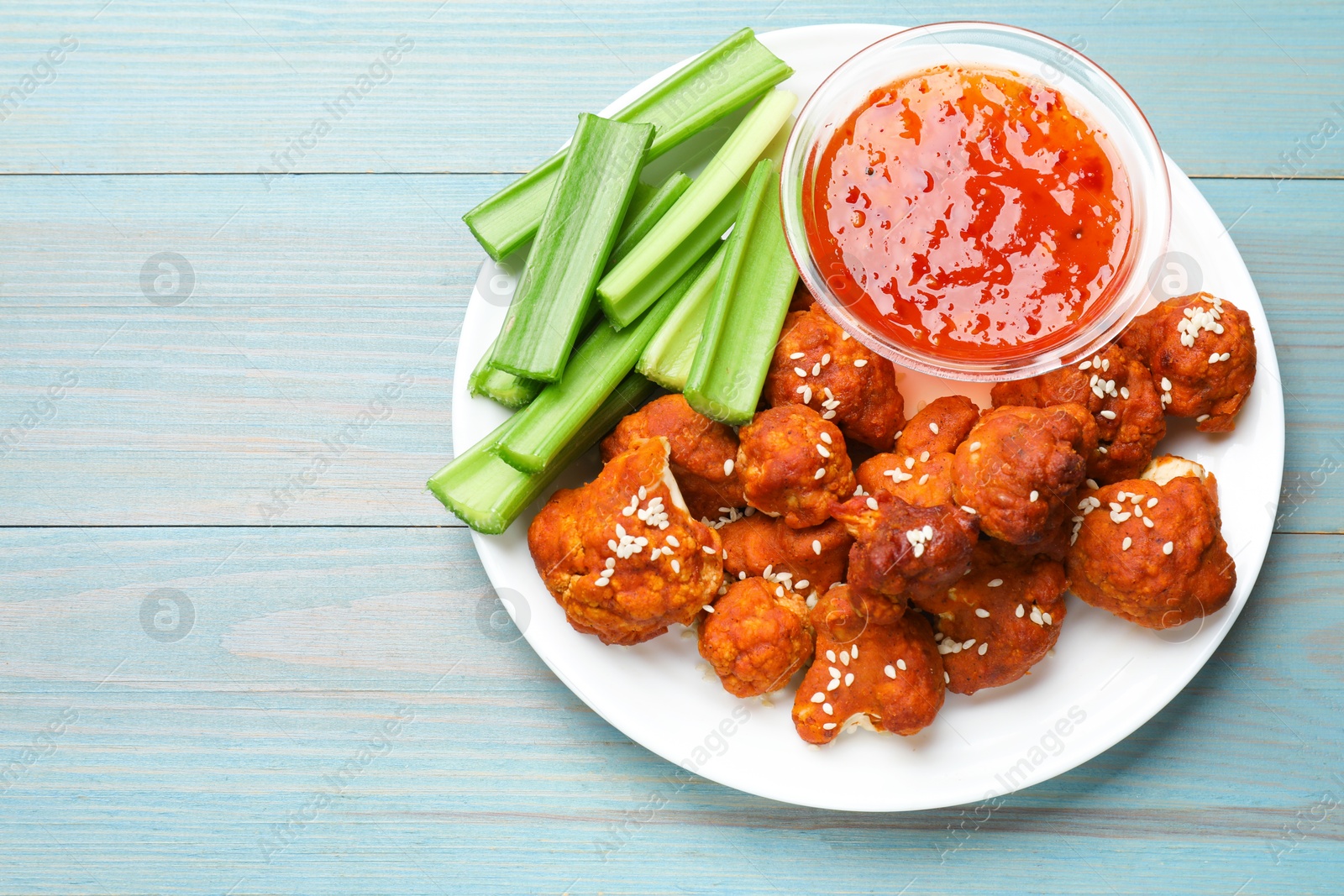 Photo of Tasty cauliflower buffalo wings, sauce and celery on light blue wooden table, top view. Space for text