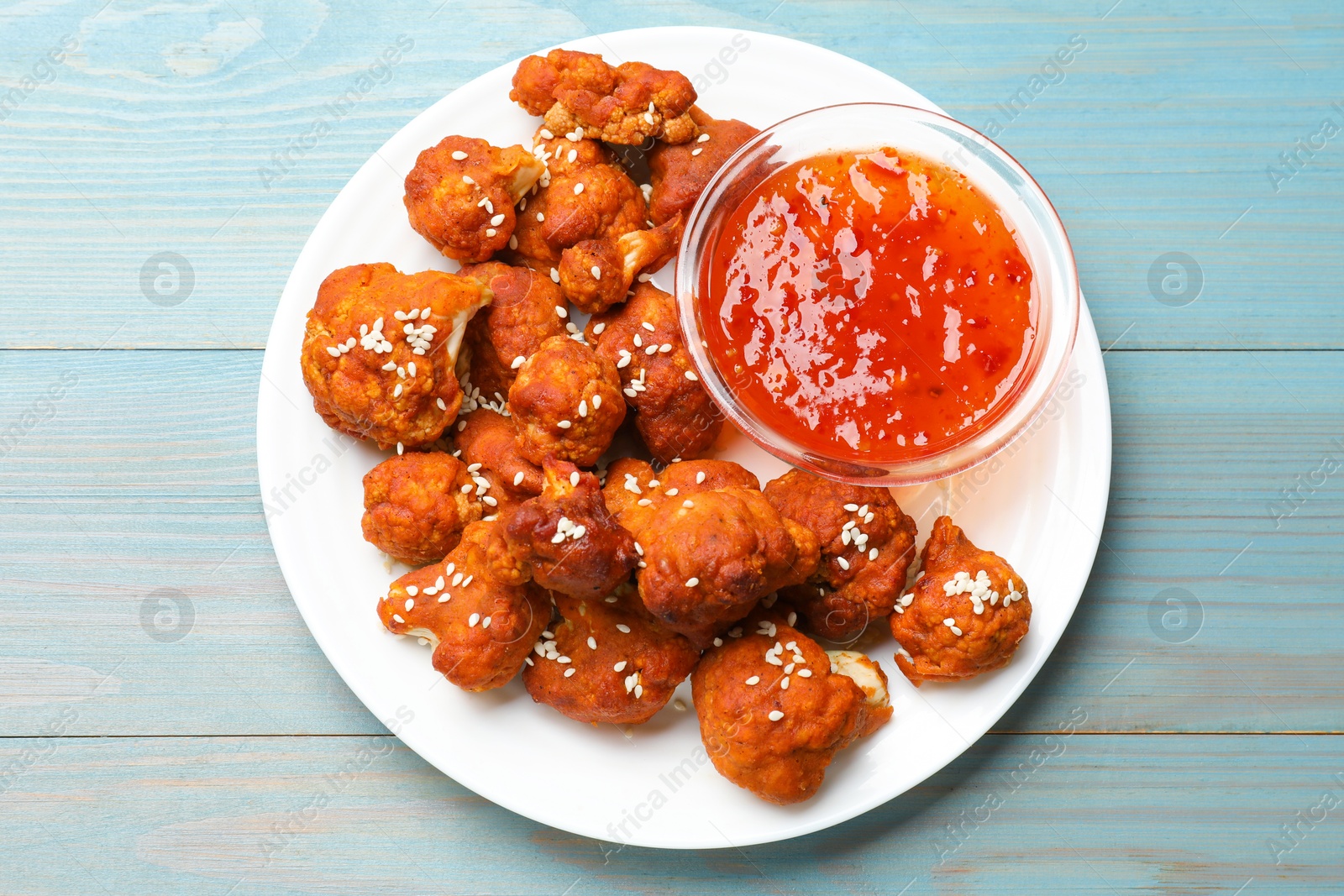 Photo of Tasty cauliflower buffalo wings and sauce on light blue wooden table, top view