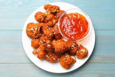 Photo of Tasty cauliflower buffalo wings and sauce on light blue wooden table, top view