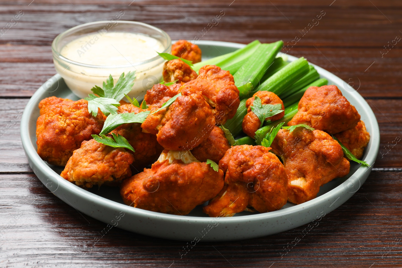 Photo of Tasty cauliflower buffalo wings, sauce and celery on wooden table, closeup