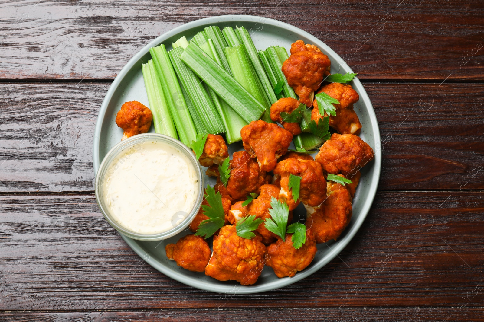 Photo of Tasty cauliflower buffalo wings, sauce and celery on wooden table, top view