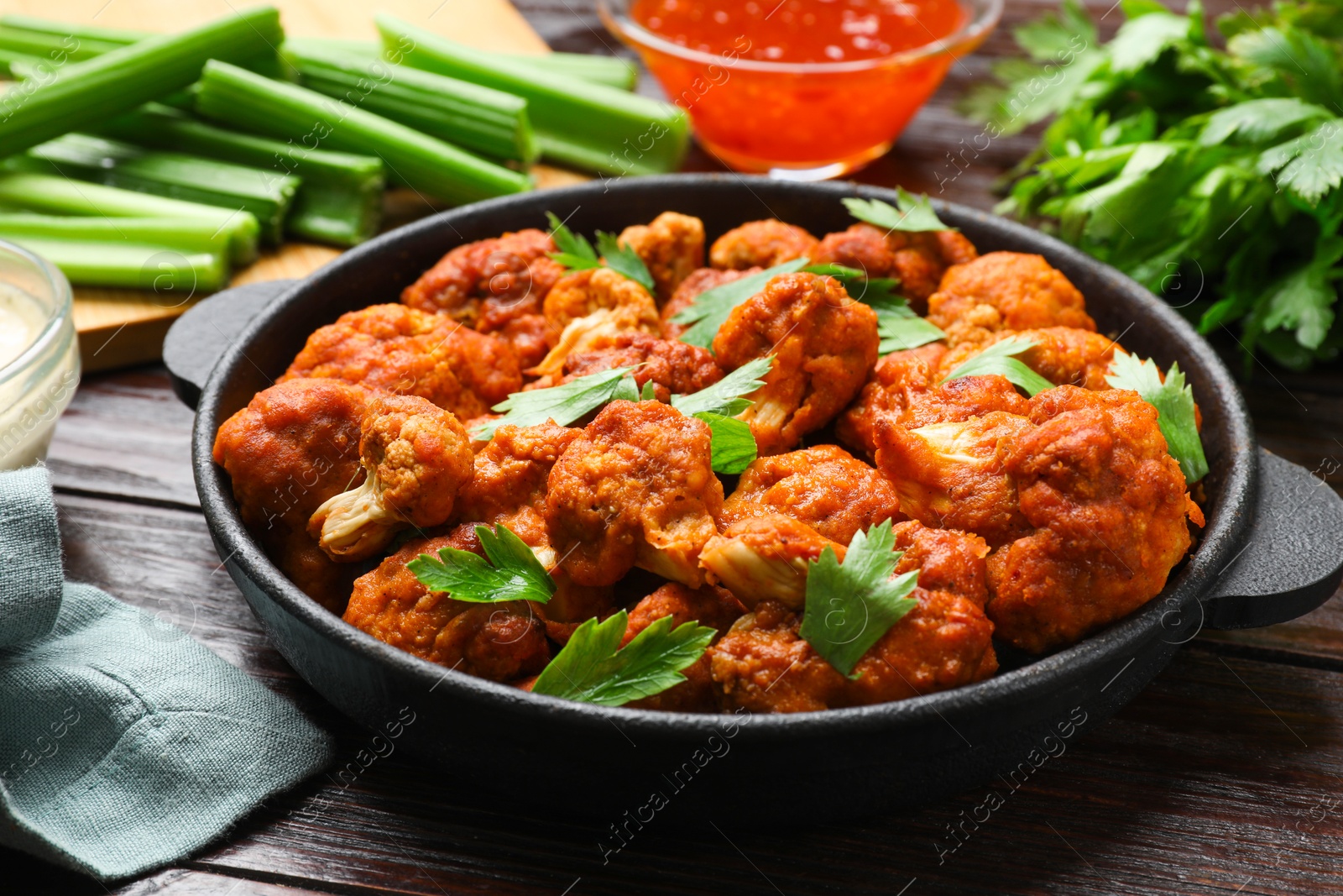 Photo of Tasty cauliflower buffalo wings, sauces and celery on wooden table, closeup