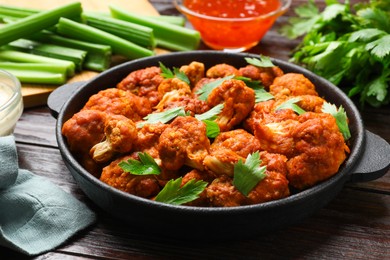 Photo of Tasty cauliflower buffalo wings, sauces and celery on wooden table, closeup