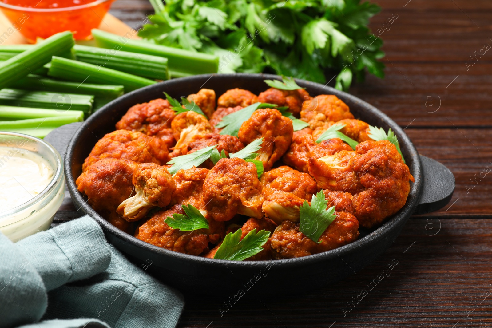 Photo of Tasty cauliflower buffalo wings, sauces and celery on wooden table, closeup