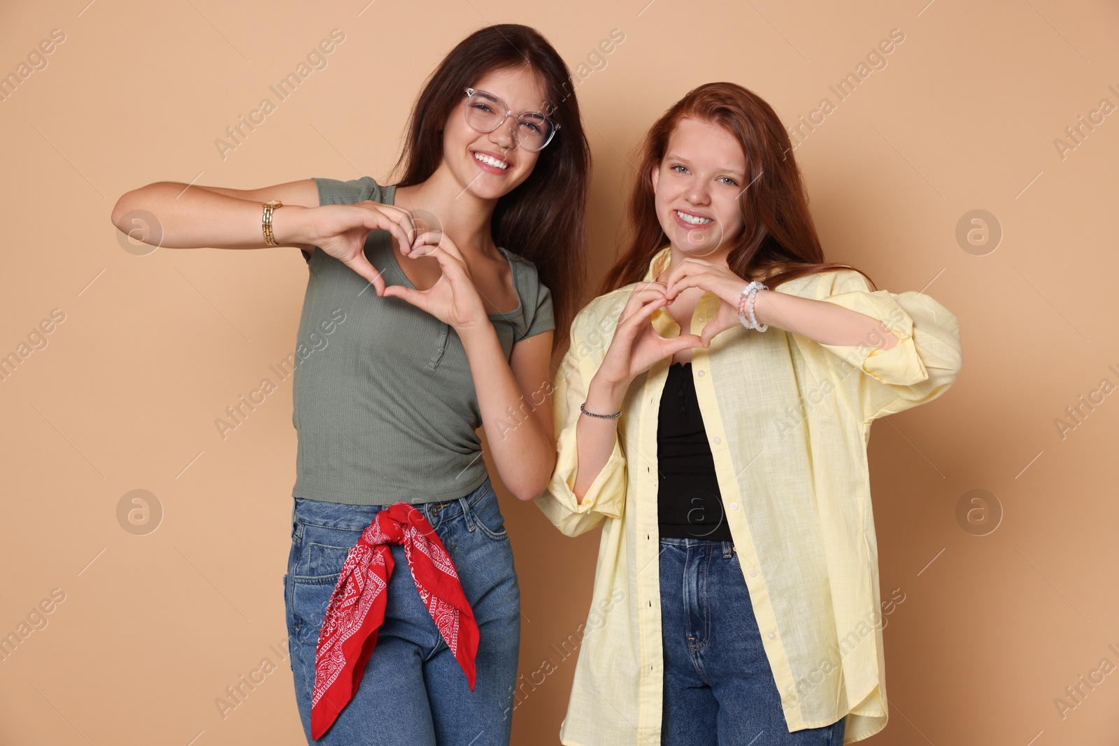 Photo of Happy teenage girls making hearts with hands on beige background