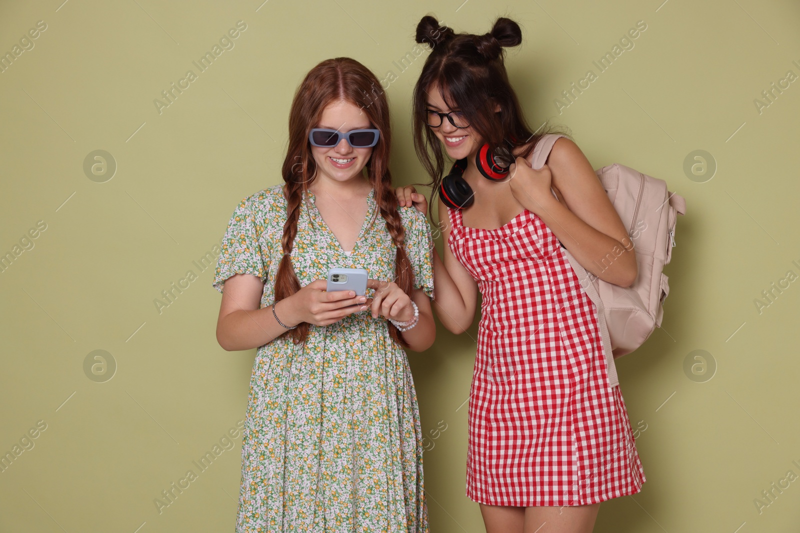 Photo of Happy teenage girls looking at smartphone on green background. Space for text