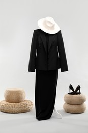 Photo of One female mannequin with dress, jacket, poufs, hat and shoes on light background