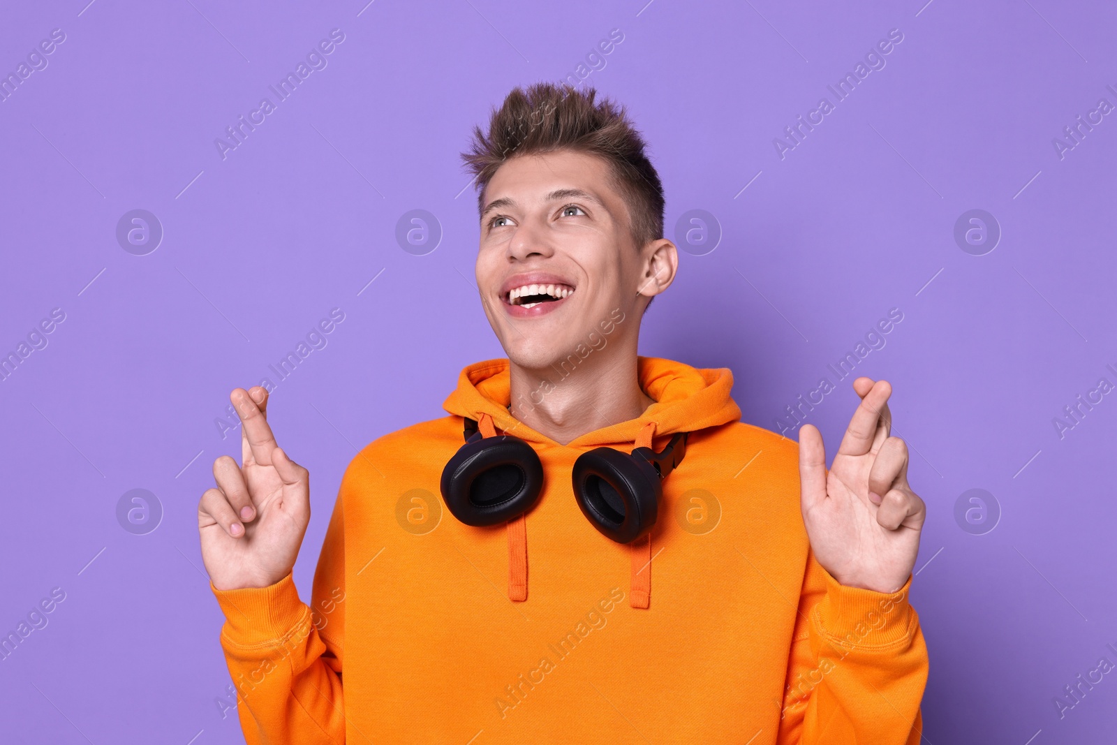 Photo of Excited young student crossing fingers on violet background. Hope for good exam result