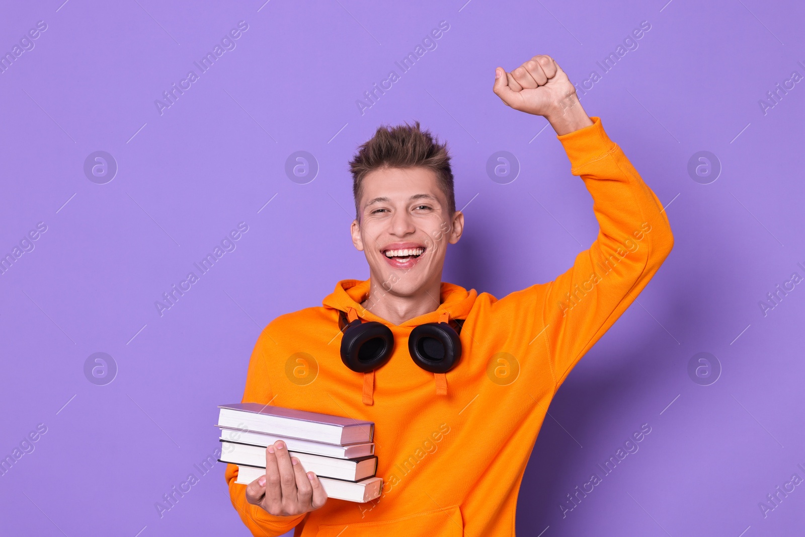 Photo of Young student with stack of books happy about his good exam result on violet background