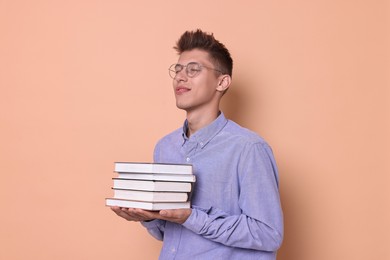 Young student with stack of books on beige background