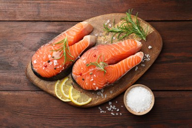 Photo of Fresh raw salmon steaks with spices, lemon and rosemary on wooden table, flat lay