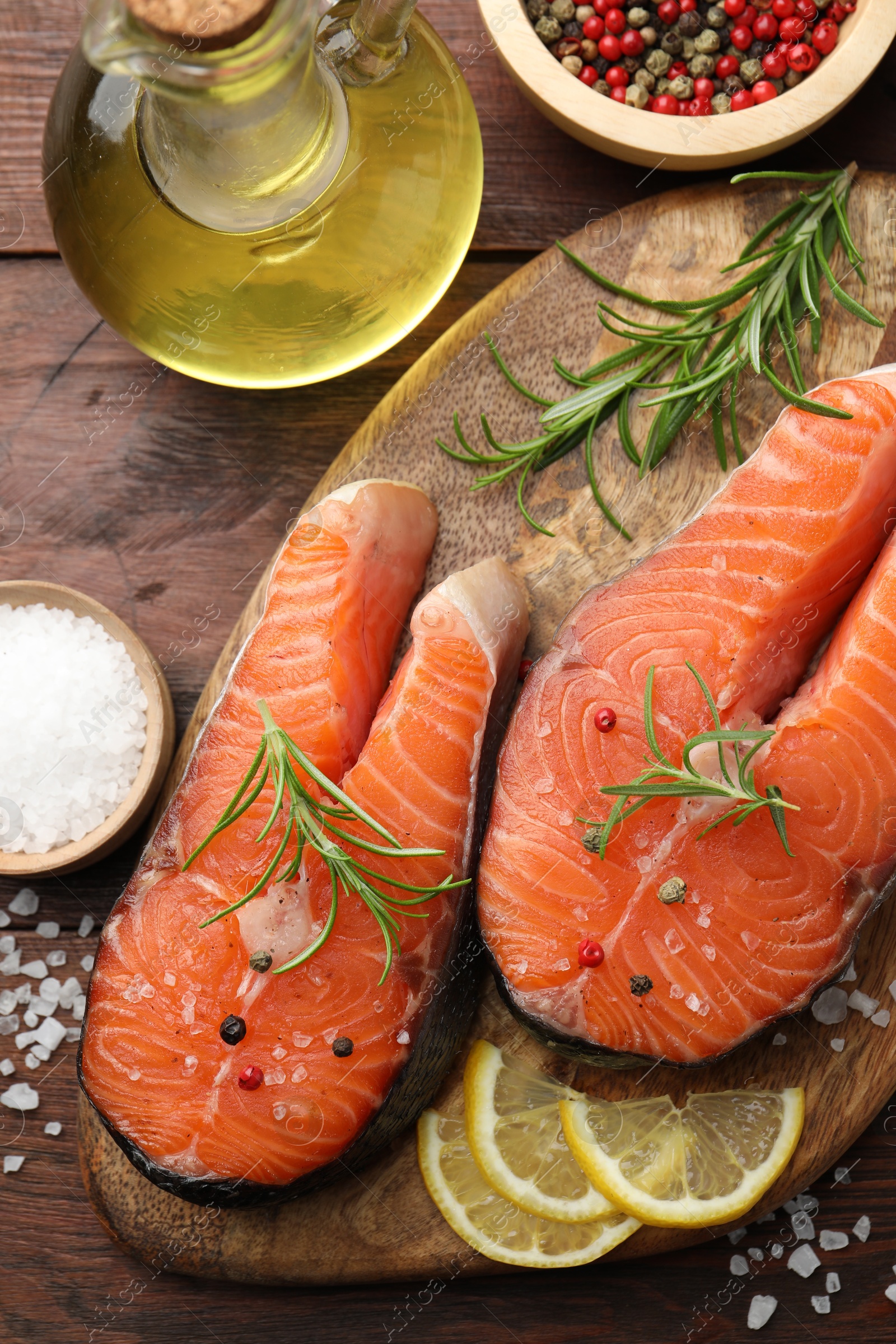 Photo of Fresh raw salmon steaks with spices, lemon, oil and rosemary on wooden table, flat lay