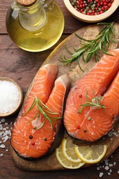 Photo of Fresh raw salmon steaks with spices, lemon, oil and rosemary on wooden table, flat lay