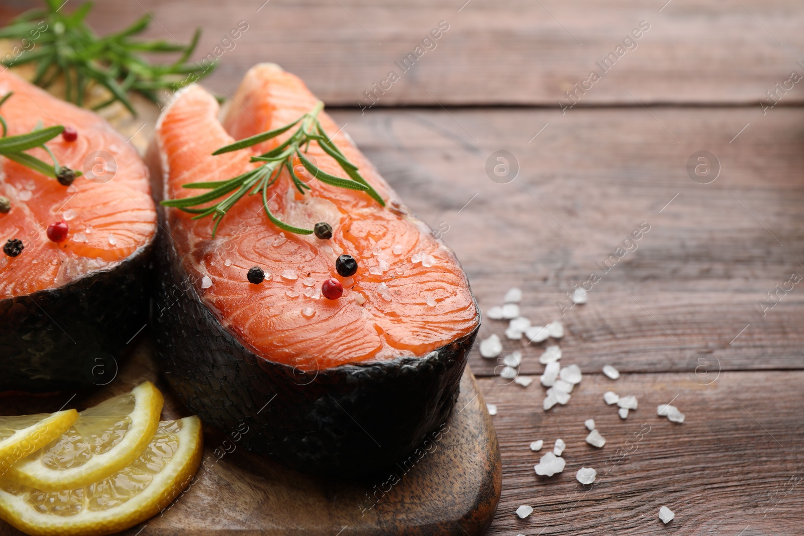 Photo of Fresh raw salmon steaks with spices, lemon and rosemary on wooden table, closeup. Space for text