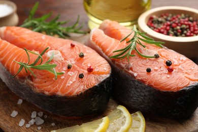 Photo of Fresh raw salmon steaks with spices, lemon and rosemary on wooden board, closeup