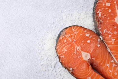 Photo of Fresh raw salmon steaks with salt on light textured table, top view. Space for text