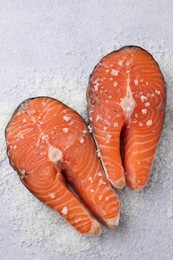 Photo of Fresh raw salmon steaks with salt on light textured table, top view