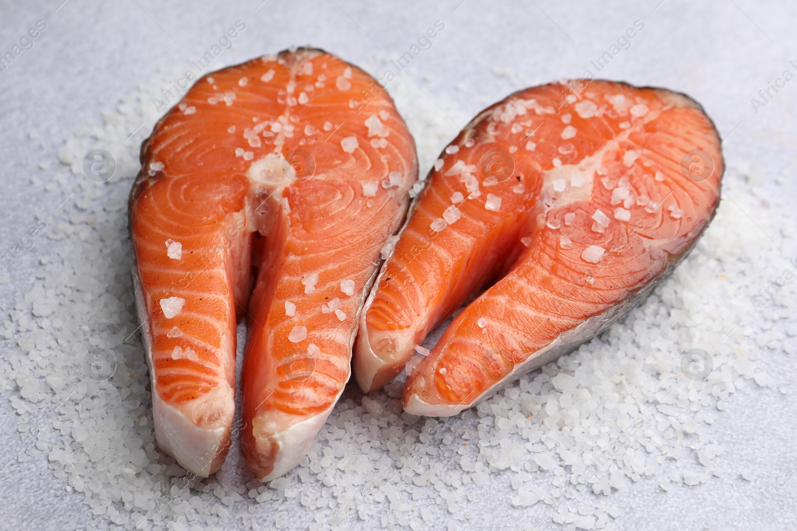 Photo of Fresh raw salmon steaks with salt on light table, closeup