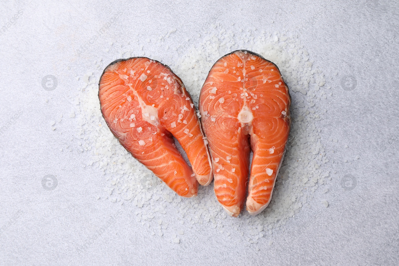 Photo of Fresh raw salmon steaks with salt on light textured table, top view