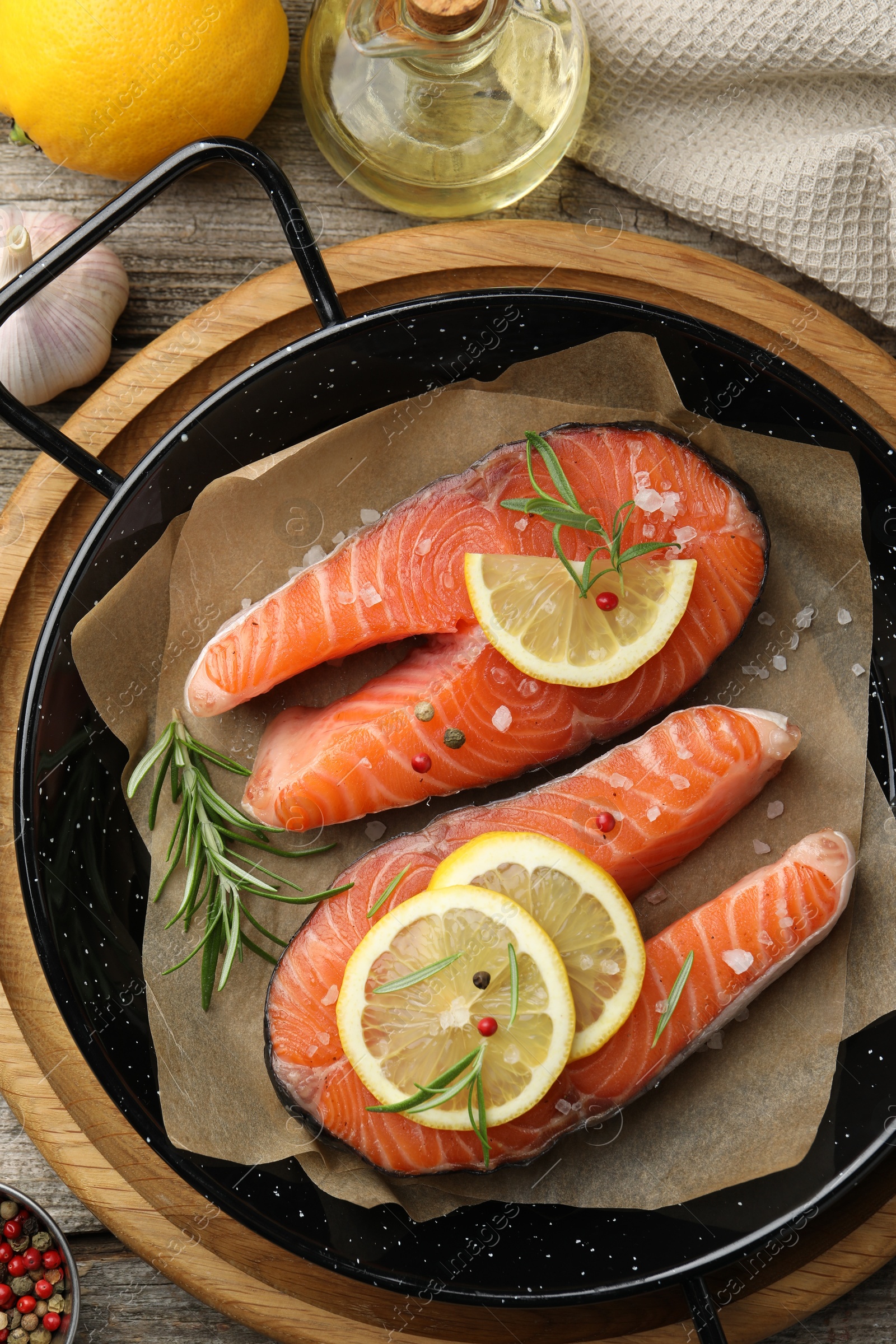 Photo of Fresh raw salmon steaks with spices in pan and products on wooden table, flat lay