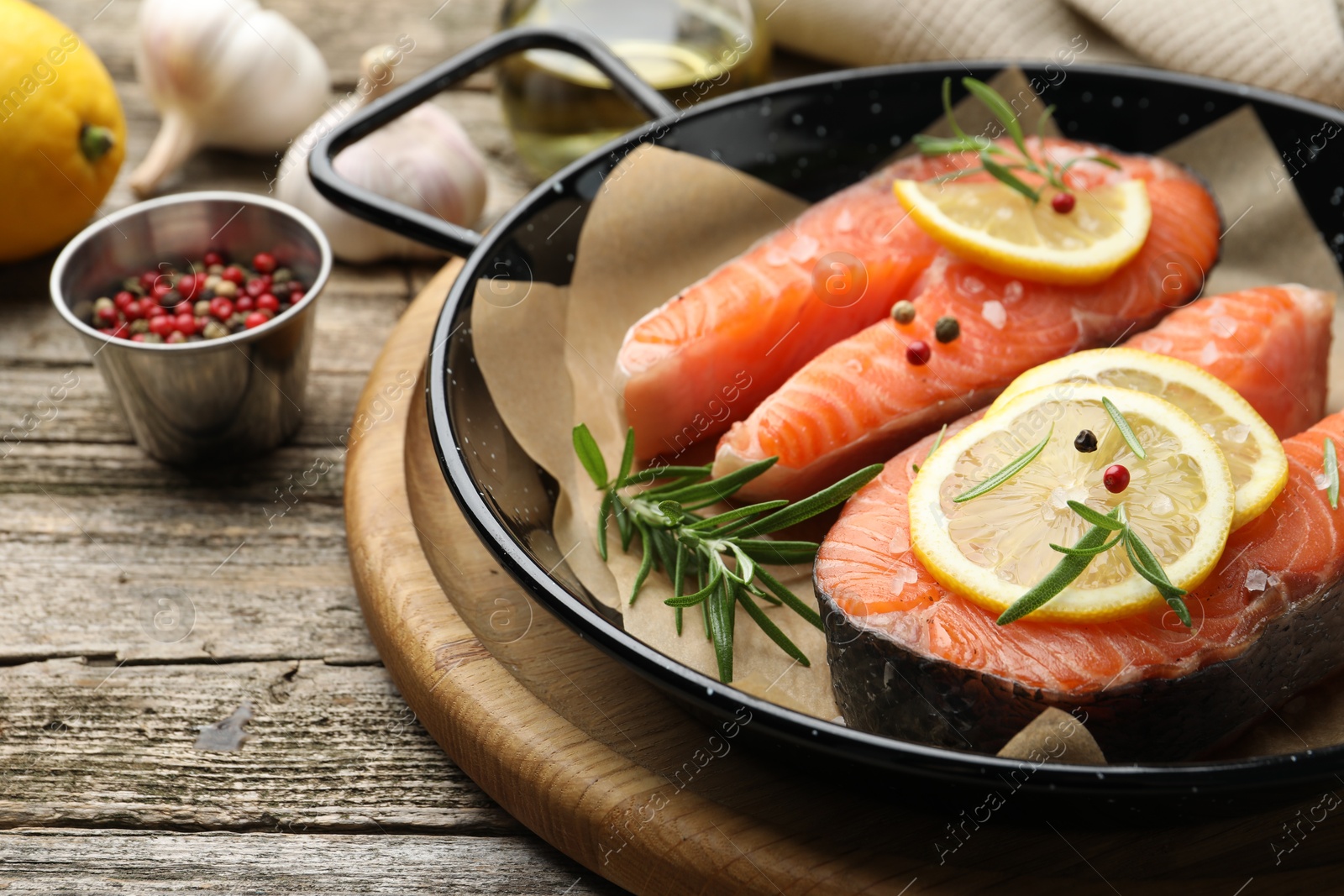 Photo of Fresh raw salmon steaks with spices in pan on wooden table, closeup