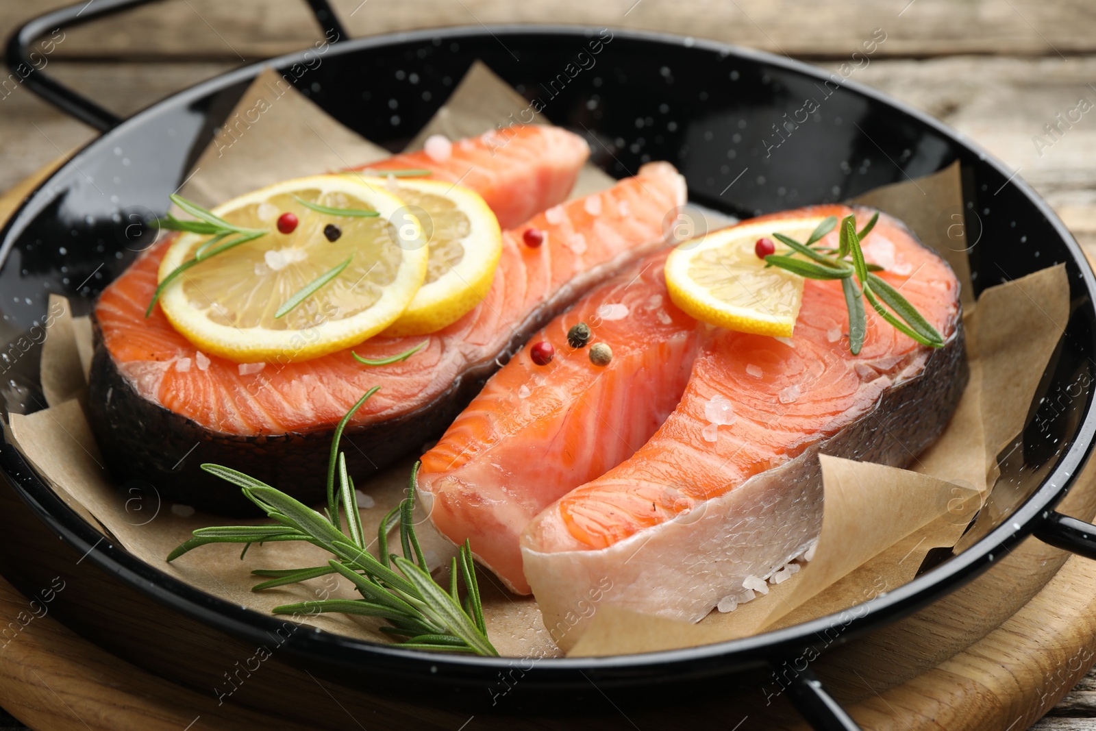 Photo of Fresh raw salmon steaks with spices in pan on wooden table, closeup