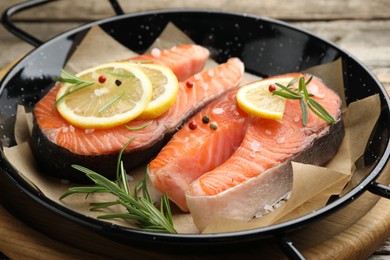 Photo of Fresh raw salmon steaks with spices in pan on wooden table, closeup