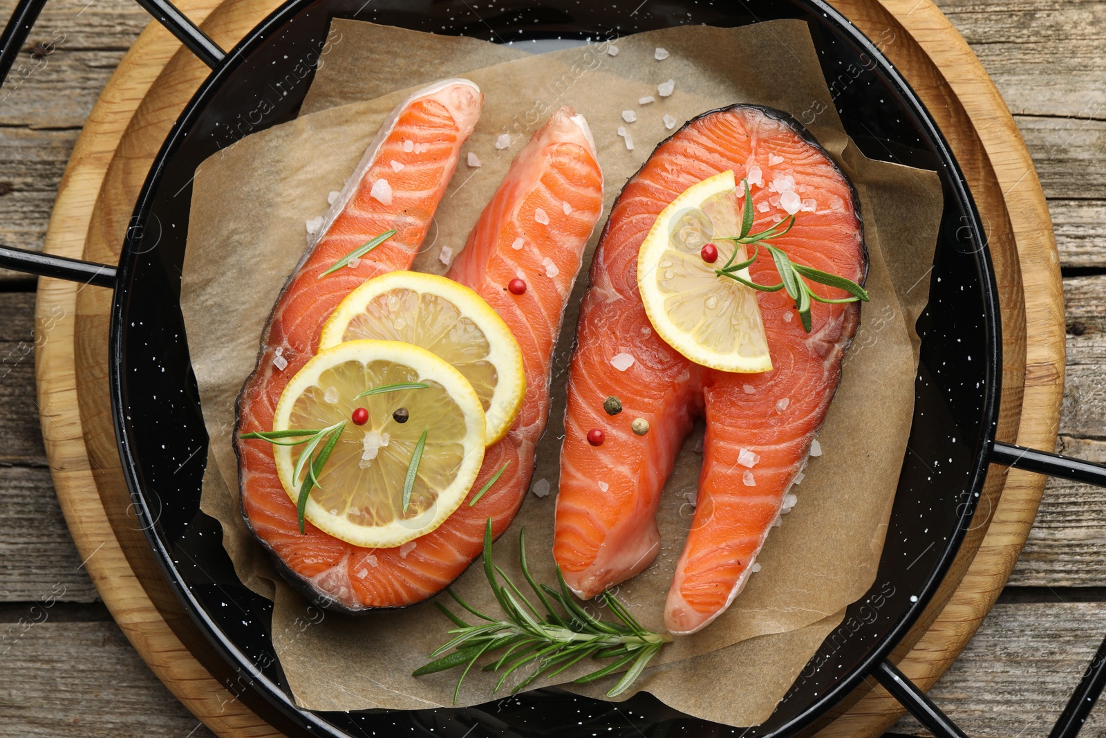 Photo of Fresh raw salmon steaks with spices in pan on wooden table, top view