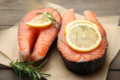 Photo of Fresh raw salmon steaks with rosemary and lemon on wooden table, closeup