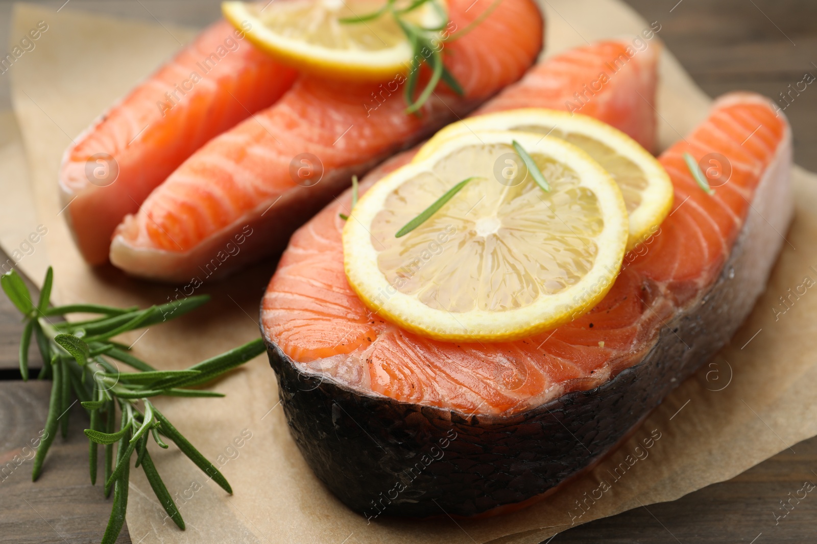 Photo of Fresh raw salmon steaks with rosemary and lemon on wooden table, closeup