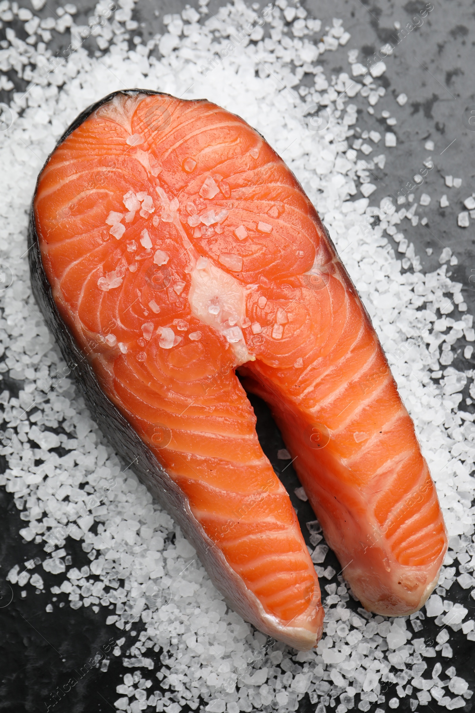 Photo of Fresh raw salmon steak with salt on dark textured table, above view