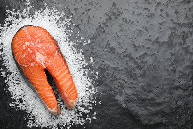 Photo of Fresh raw salmon steak with salt on dark textured table, top view. Space for text