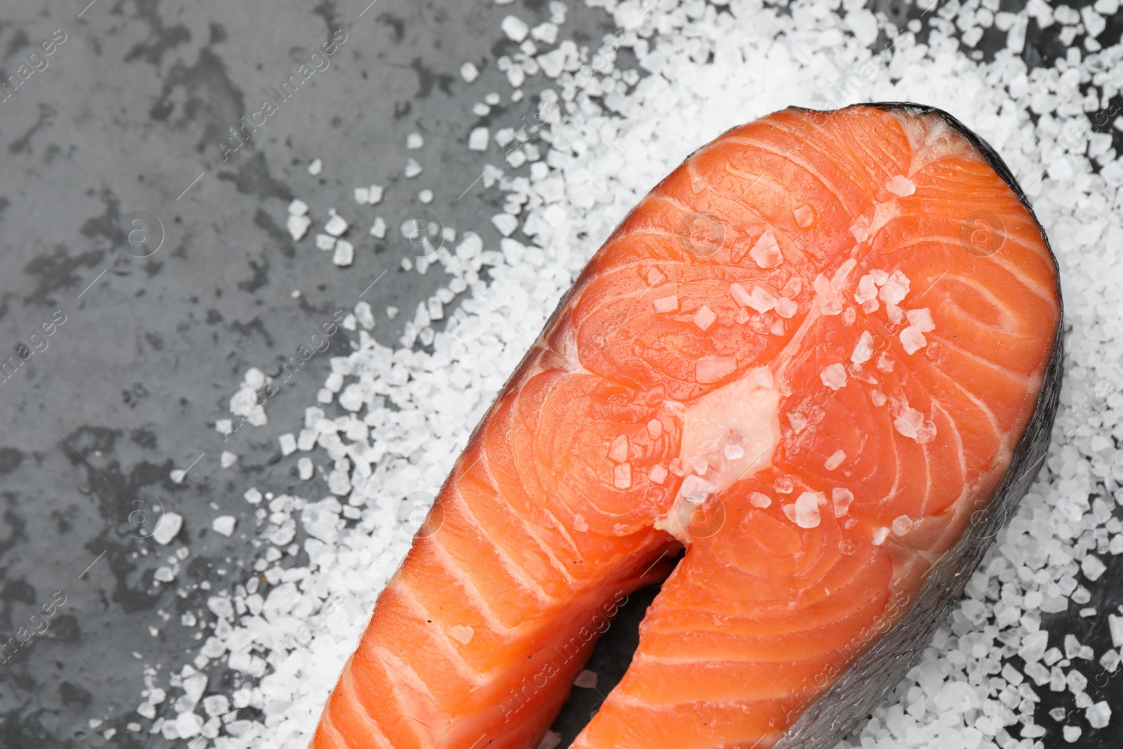 Photo of Fresh raw salmon steak with salt on dark textured table, above view. Space for text