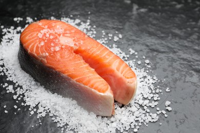 Photo of Fresh raw salmon steak with salt on dark textured table, closeup