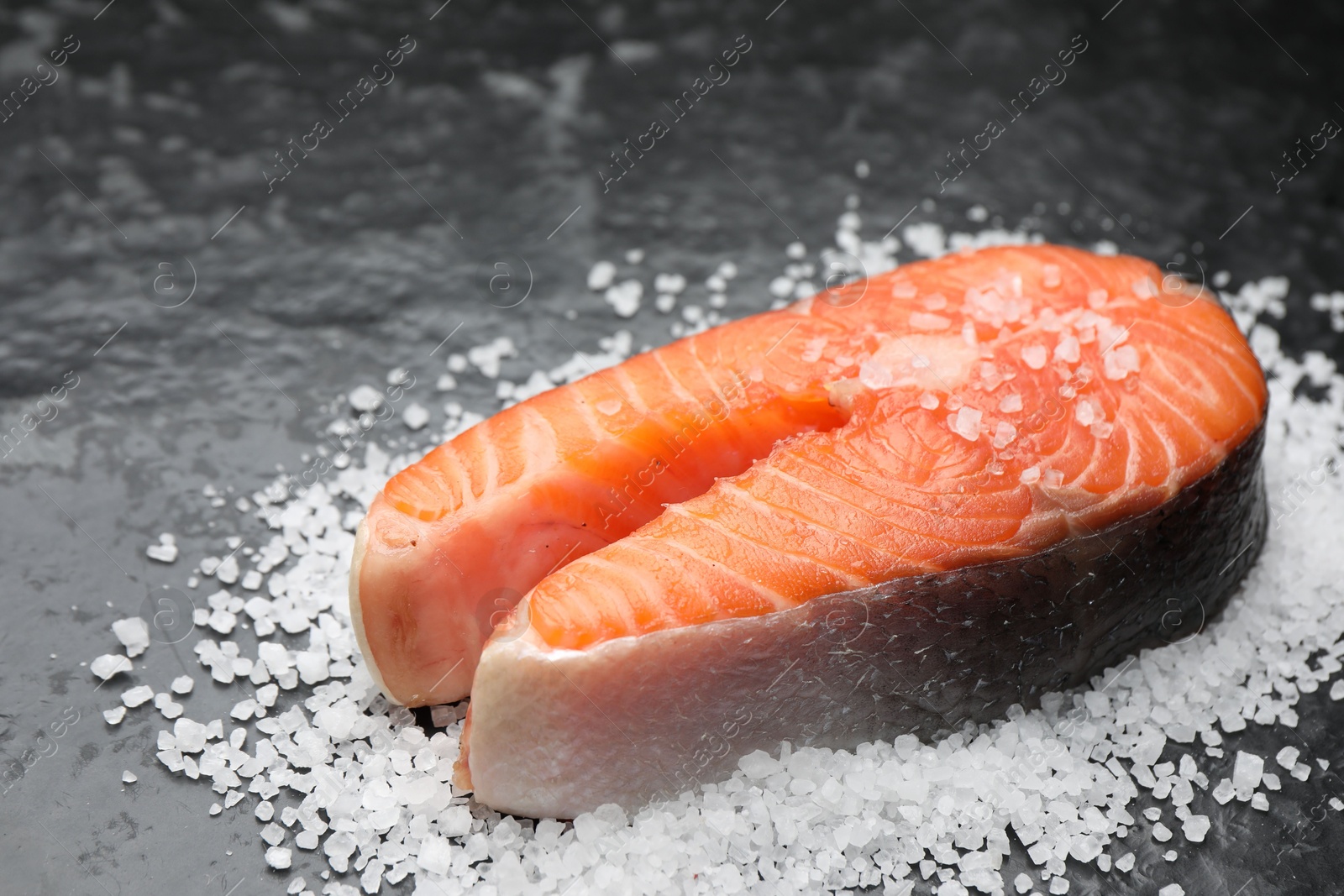 Photo of Fresh raw salmon steak with salt on dark textured table, closeup