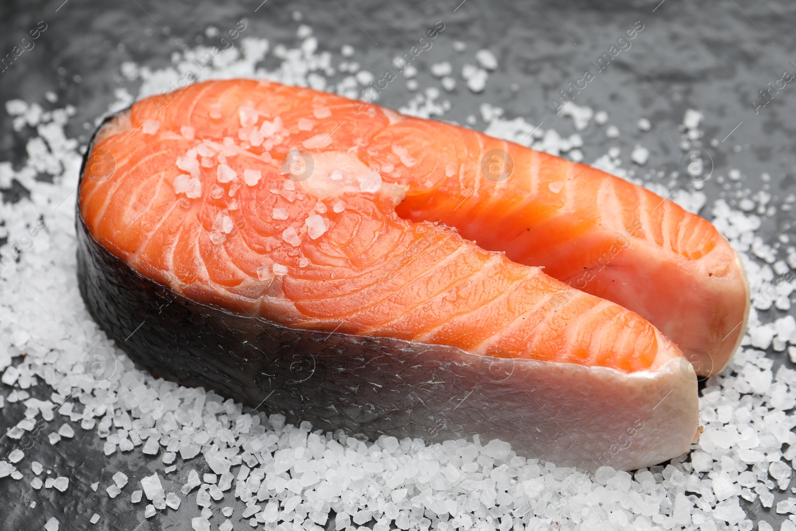 Photo of Fresh raw salmon steak with salt on dark textured table, closeup