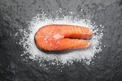 Photo of Fresh raw salmon steak with salt on dark textured table, above view