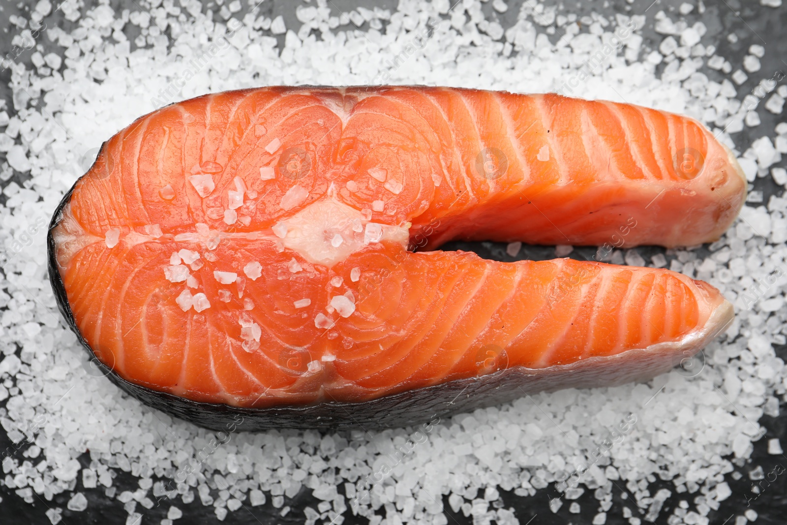 Photo of Fresh raw salmon steak with salt on dark table, above view